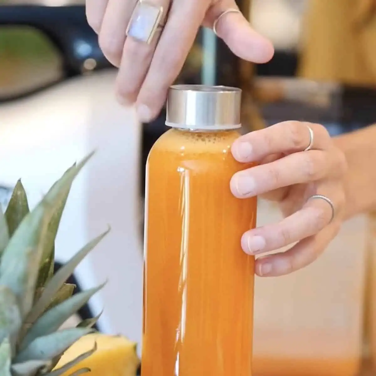 Glass bottle filled with fresh homemade carrot juice with pineapple orange and lemon.