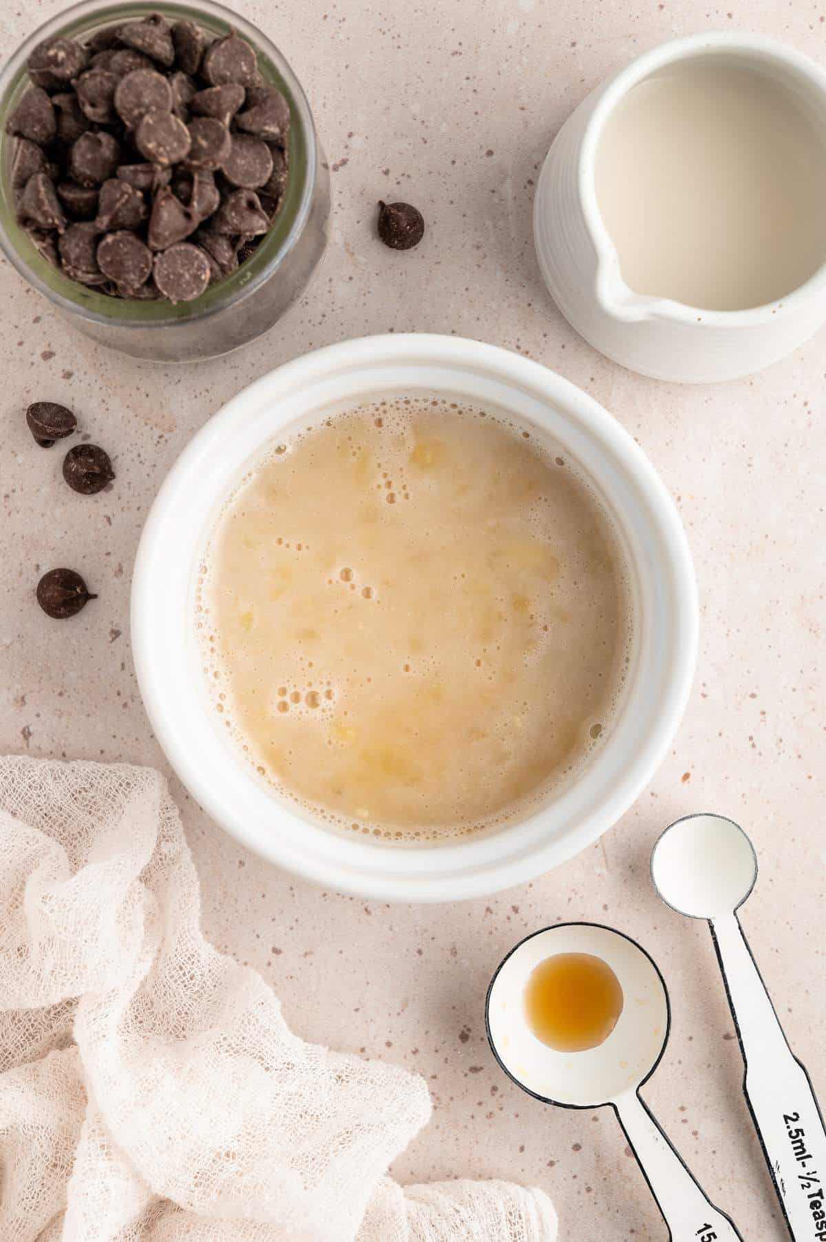Mashed banana, plant-based milk, vegan butter, and vanilla in a bowl.