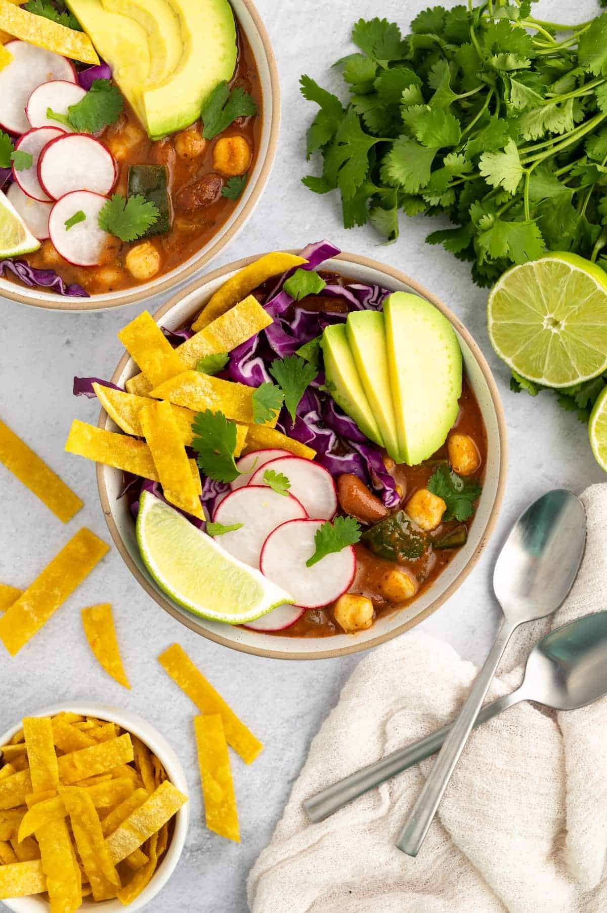 A bowl of garnished vegan pozole with cilantro and tortilla strips on the sides.