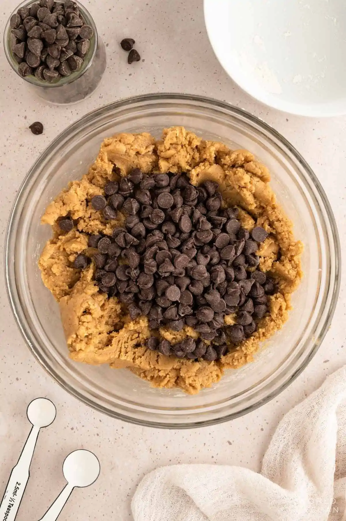 Chocolate chip cookie dough in a glass bowl with chocolate chips added in.