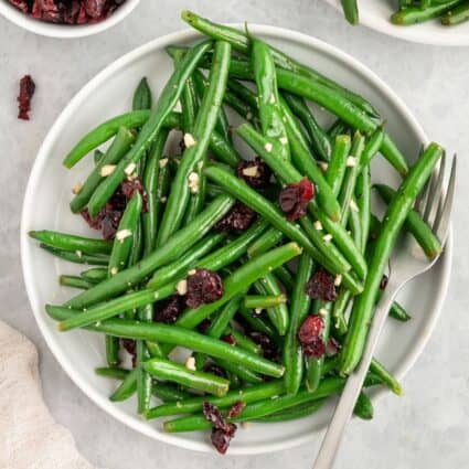 A plate of garlic green beans with cranberries on a white plate.