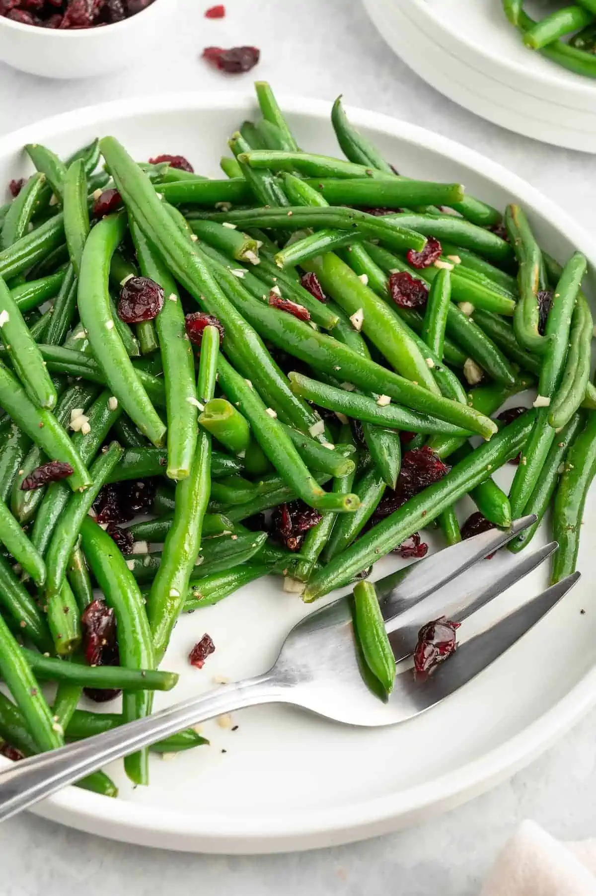 A plate of garlic green beans with cranberries on a white plate with a fork.