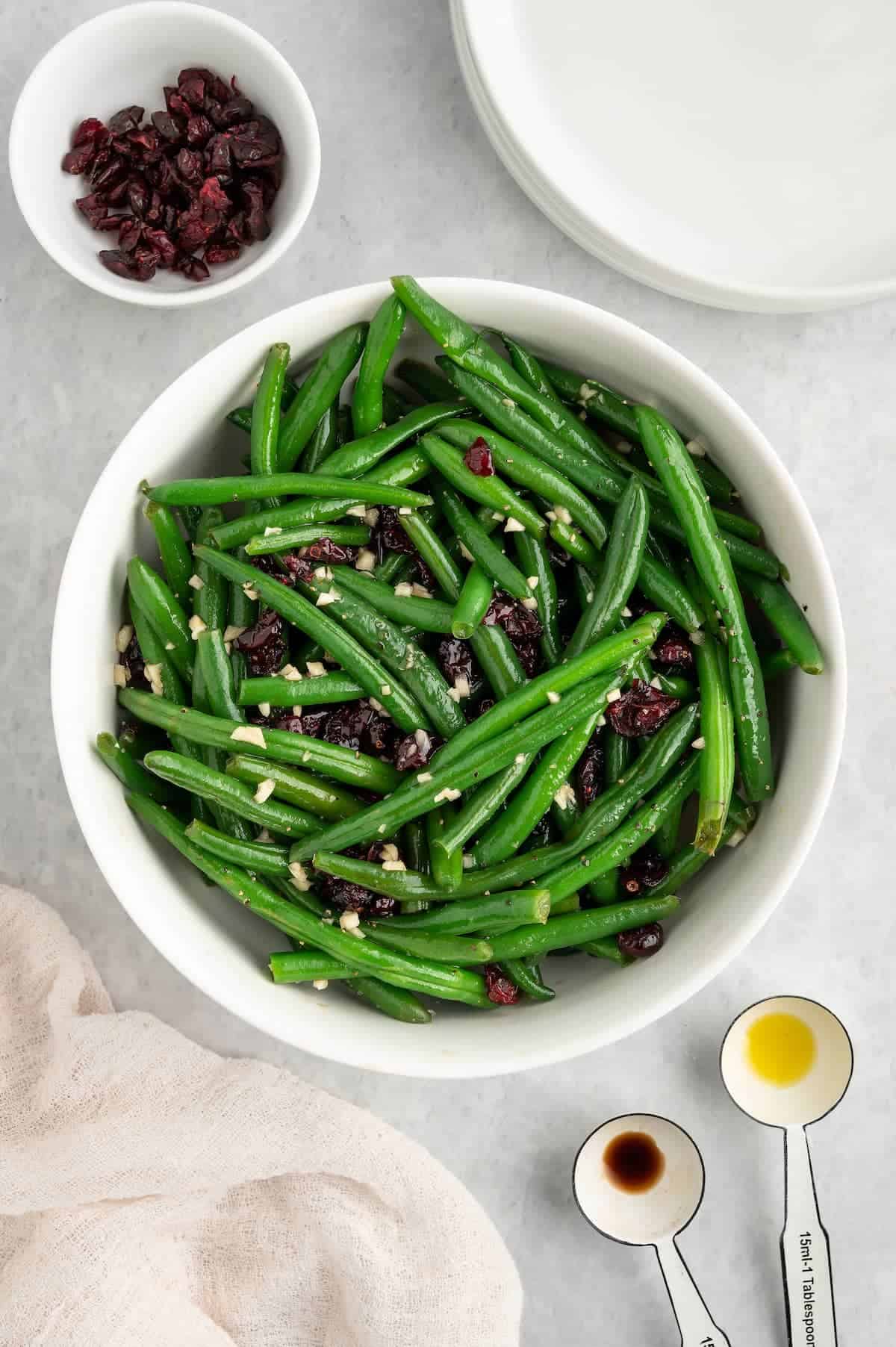 A bowl of green beans in a white bowl with dried cranberries.