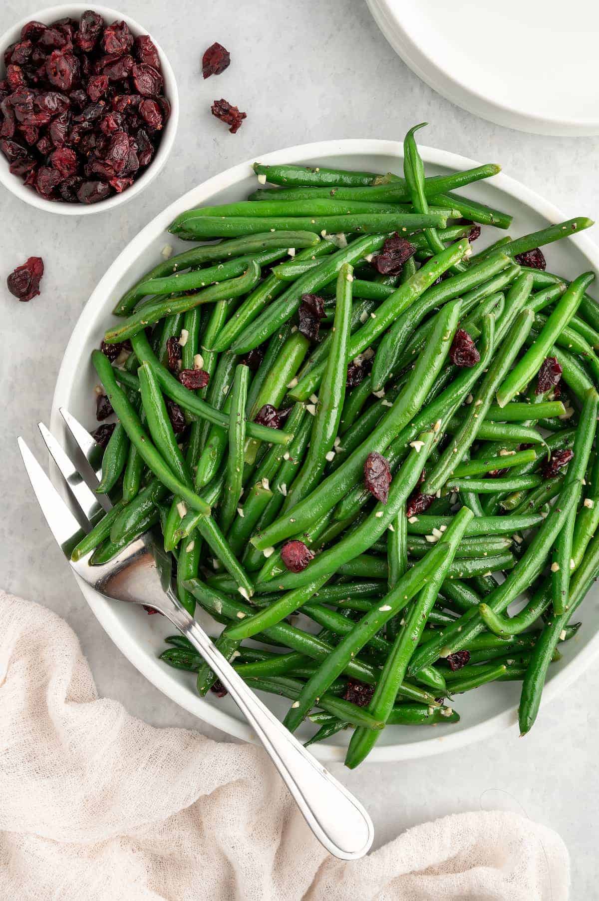 Garlic green beans with cranberries on a white plate, with a small bowl of dried cranberries to the side.