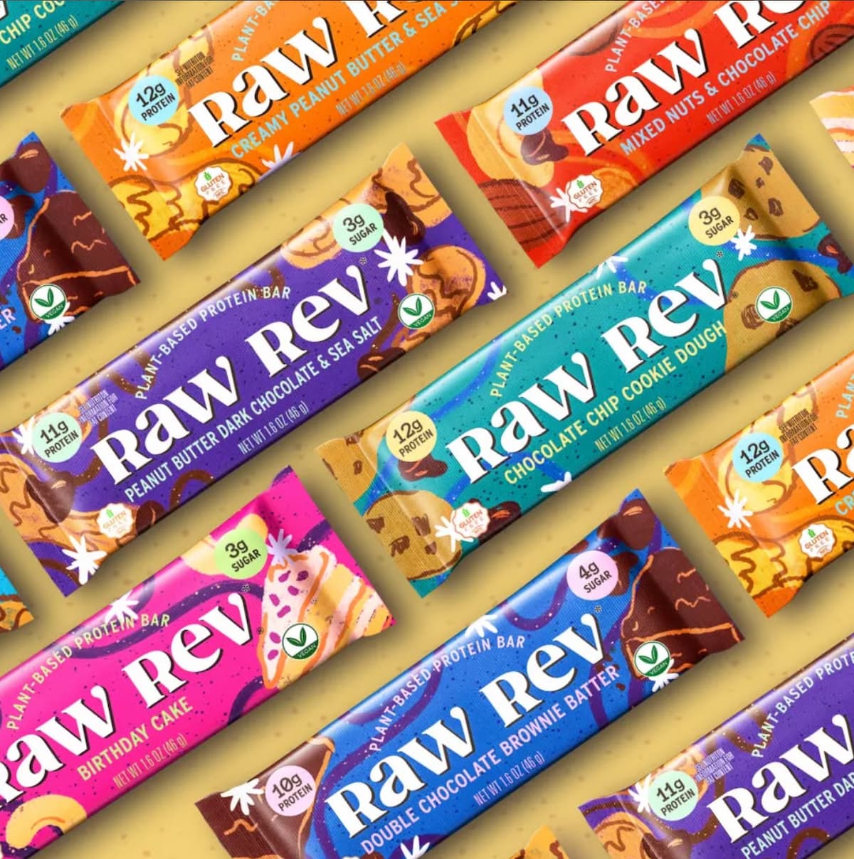 A selection of Raw Rev plant-based protein bars lined up diagonally across a light brown background. 