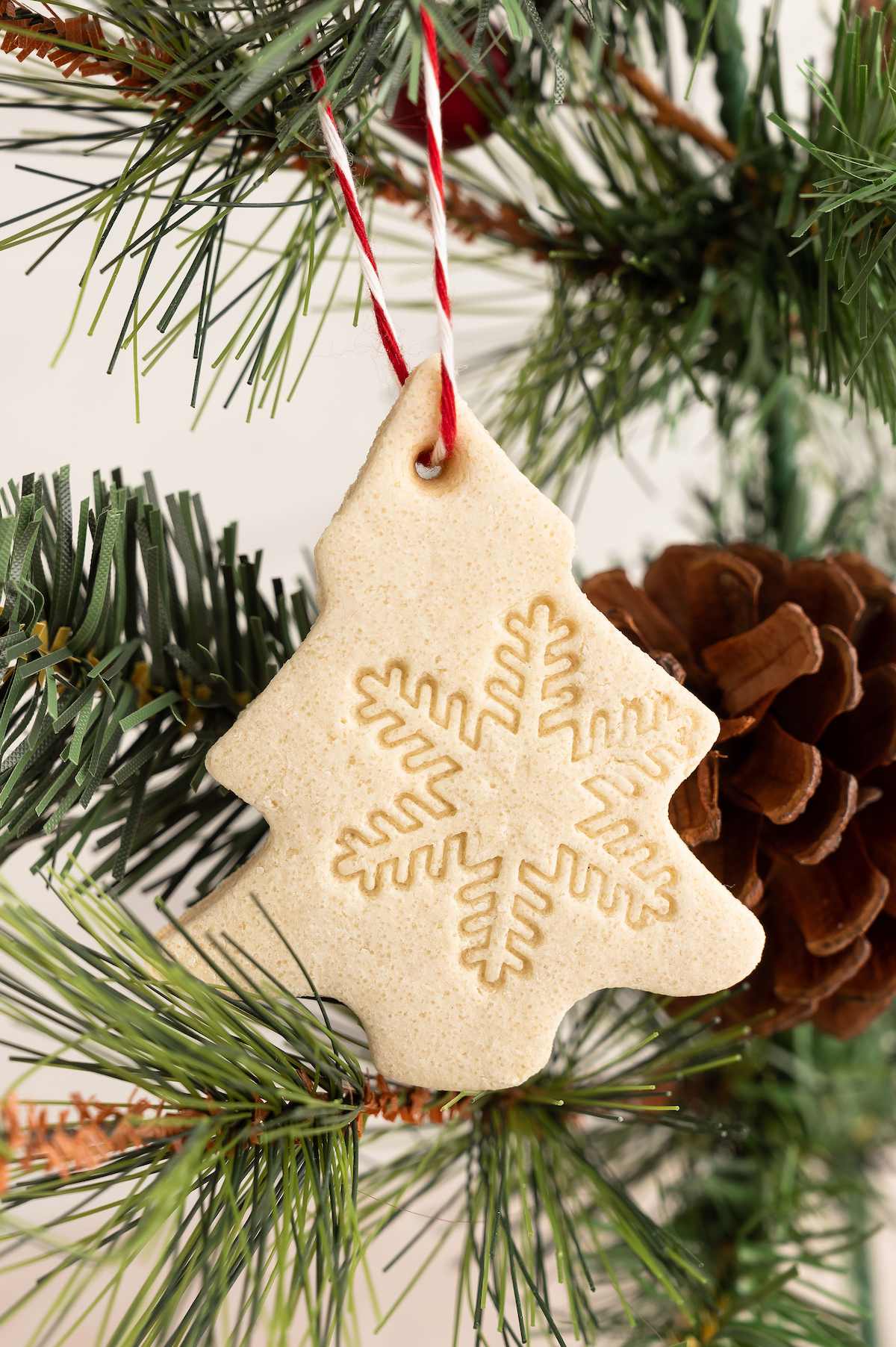 Salt dough ornament shaped like a Christmas tree, hanging on a tree branch.