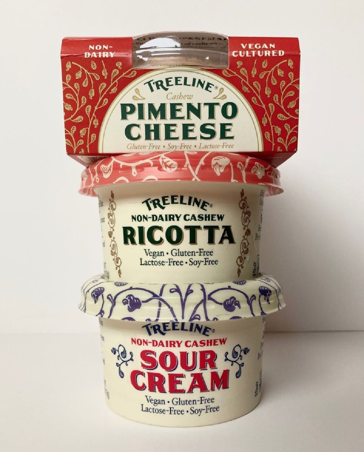 A stack of three containers of Treeline Plant-Based Cheese starting with pimento, then ricotta and finally sour cream on the bottom against a white background. 