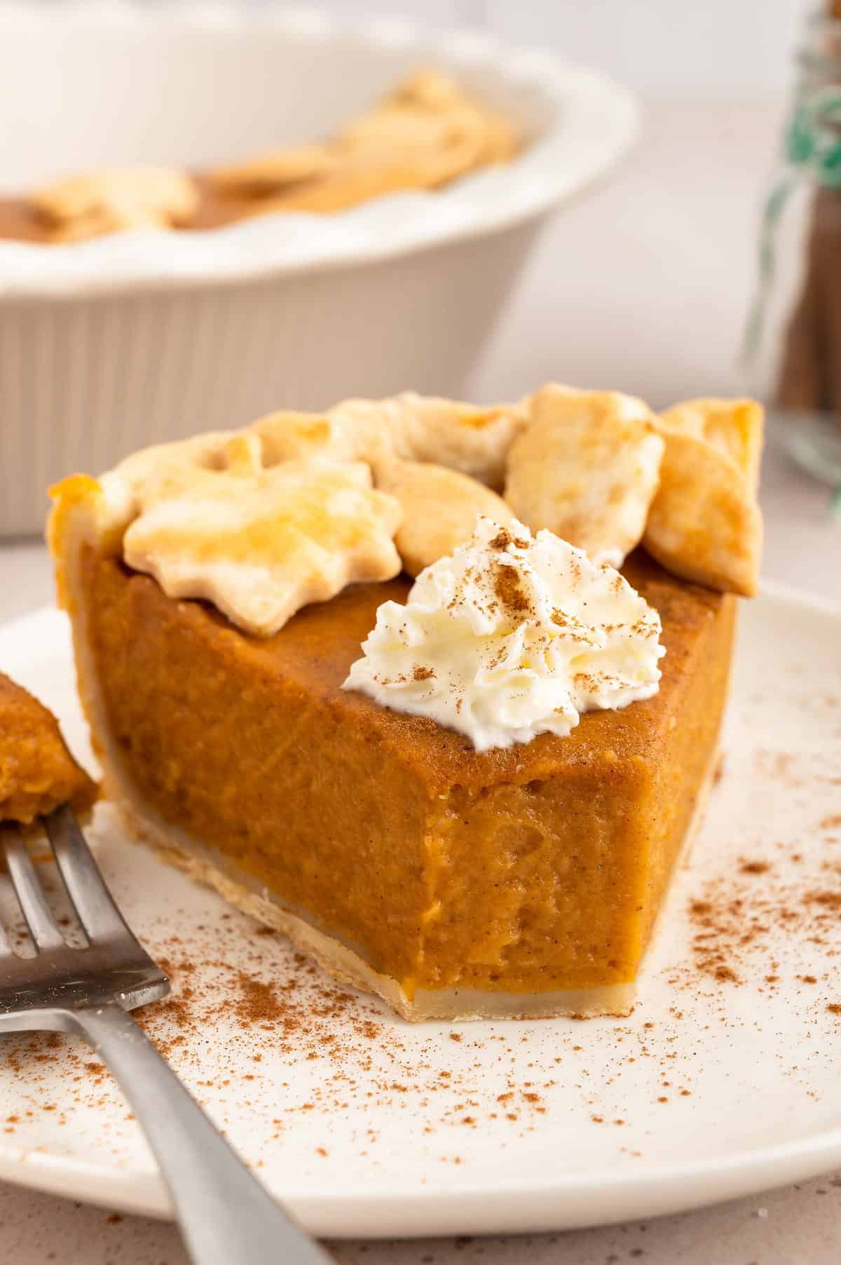 Vegan sweet potato pie on a plate and decorated with pastry leaves and topped with coconut whipped cream and a bite missing.