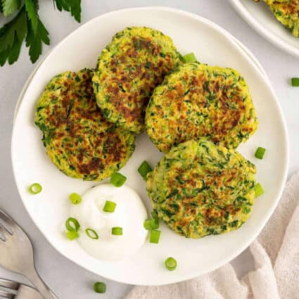 Vegan zucchini fritters on a plate with a dollop of vegan sour cream.