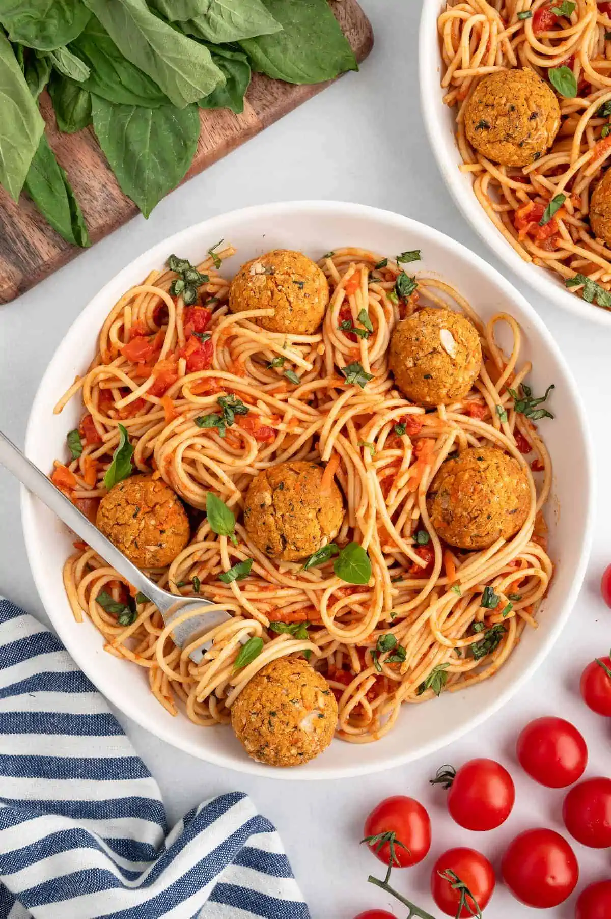 A bowl of pasta with sauce, veggie meatballs, and basil garnish with a fork.
