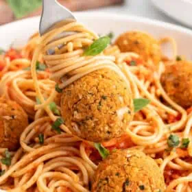 Pasta twirled on a fork with a meatball on top over a serving bowl.