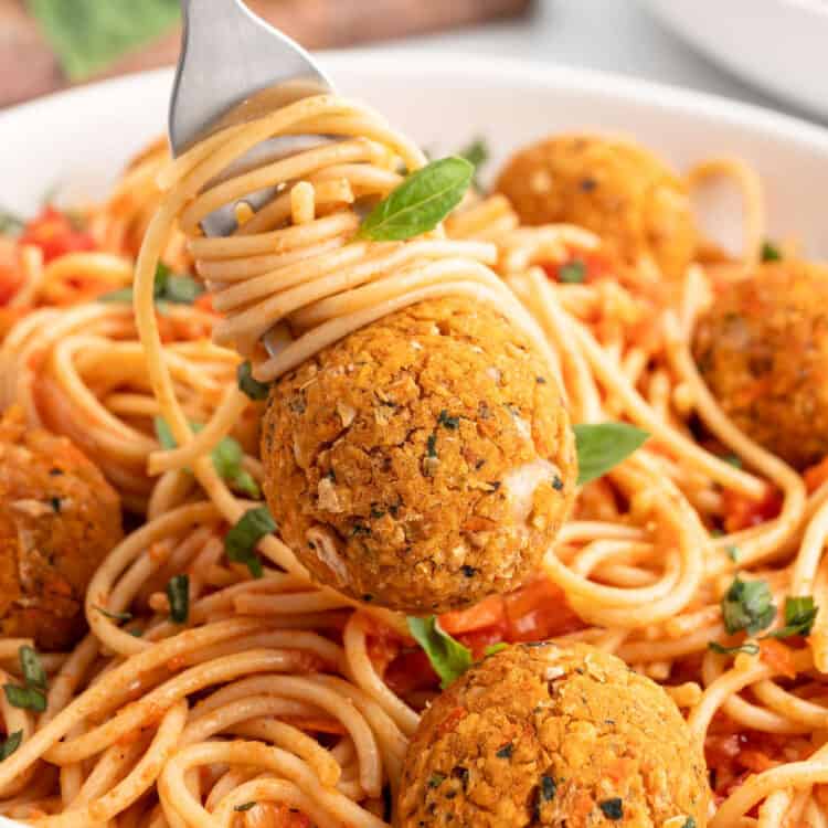 Pasta twirled on a fork with a meatball on top over a serving bowl.