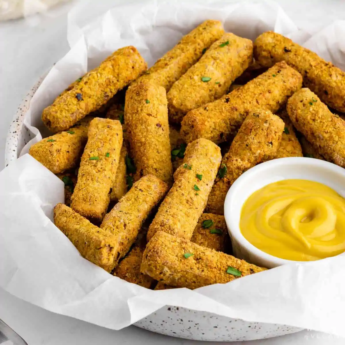 Bowl of crispy tofu fries made in the air fryer with yellow mustard.