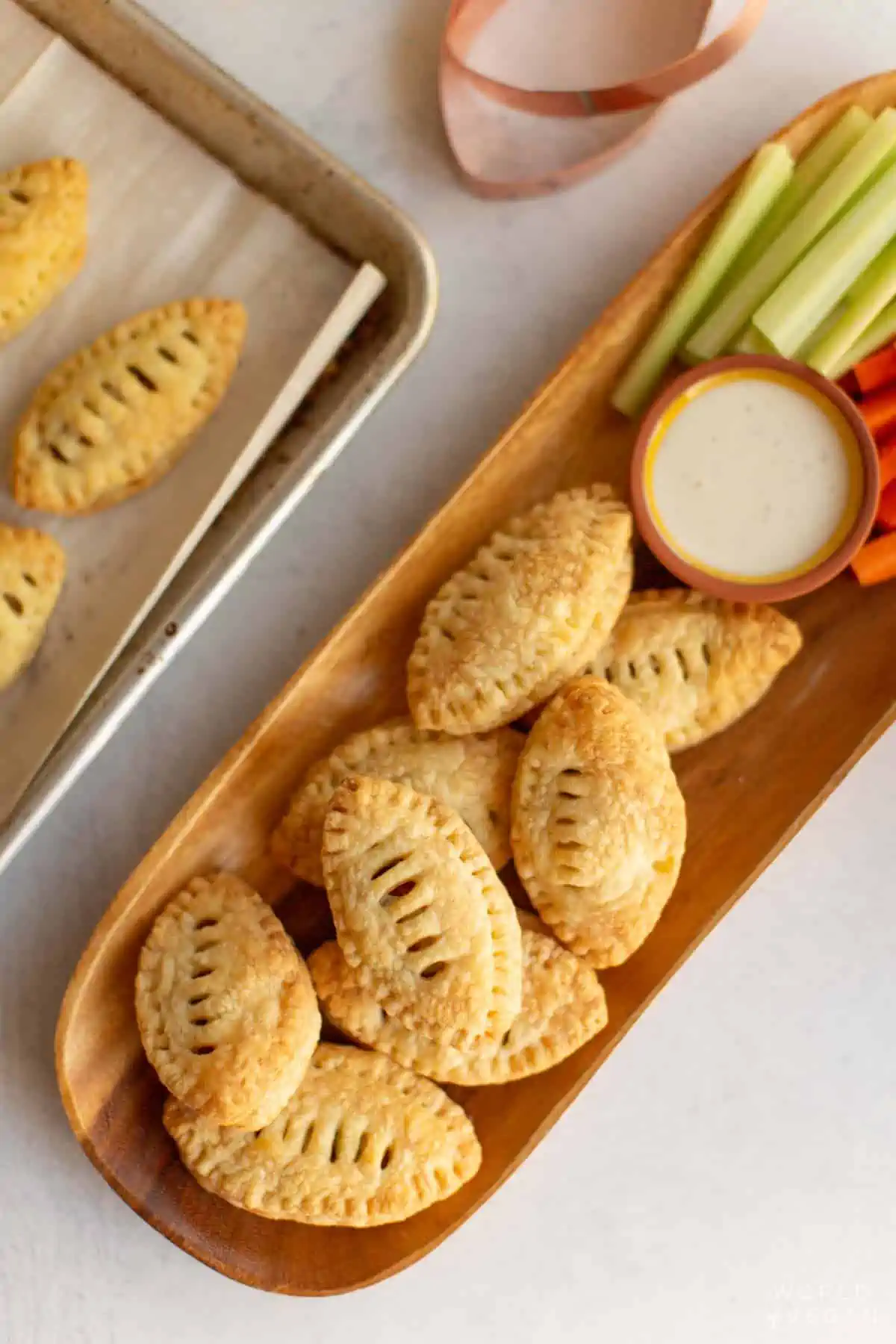 Baked football shaped puff pastry appetizer on a plate with celery and carrots. 