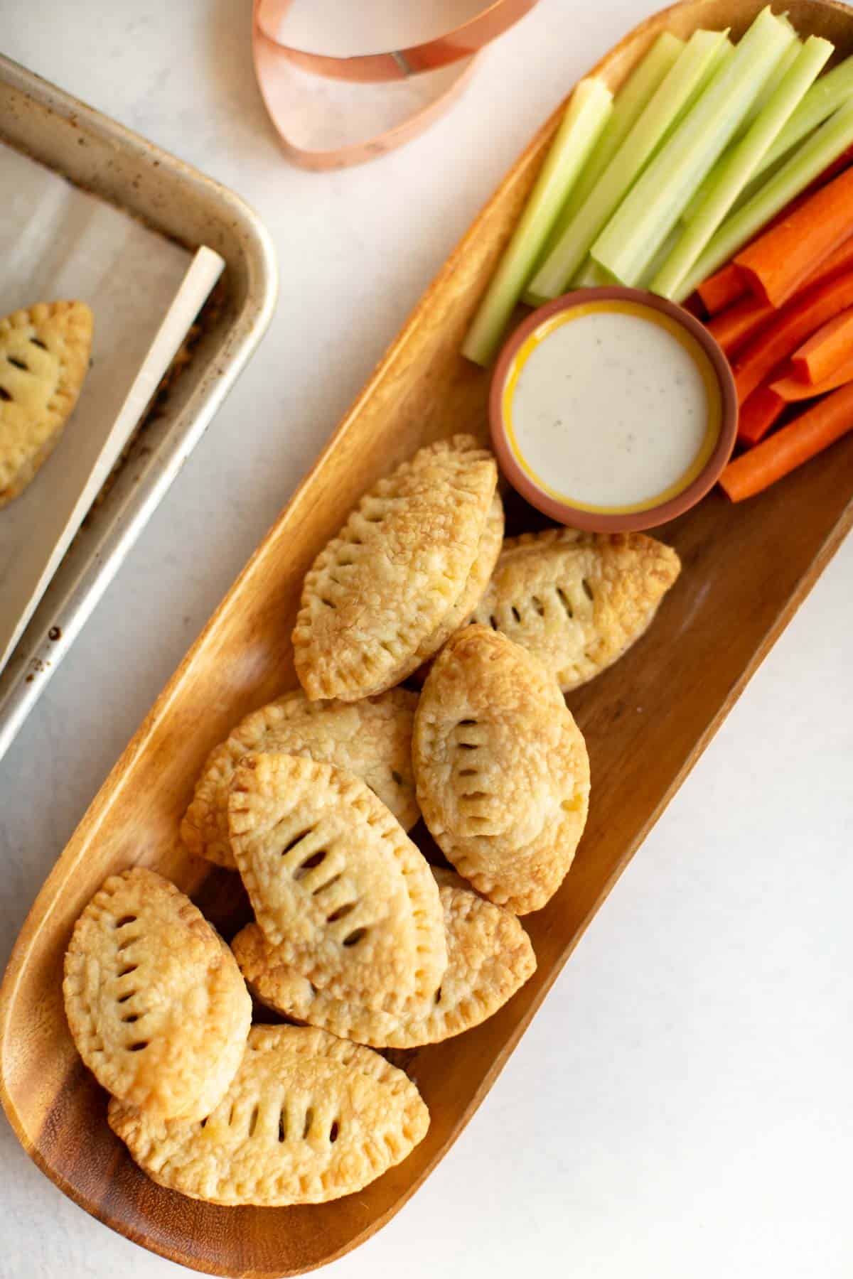 Football puff pastry appetizers on a plate served with vegan dip, celery, and carrots. 