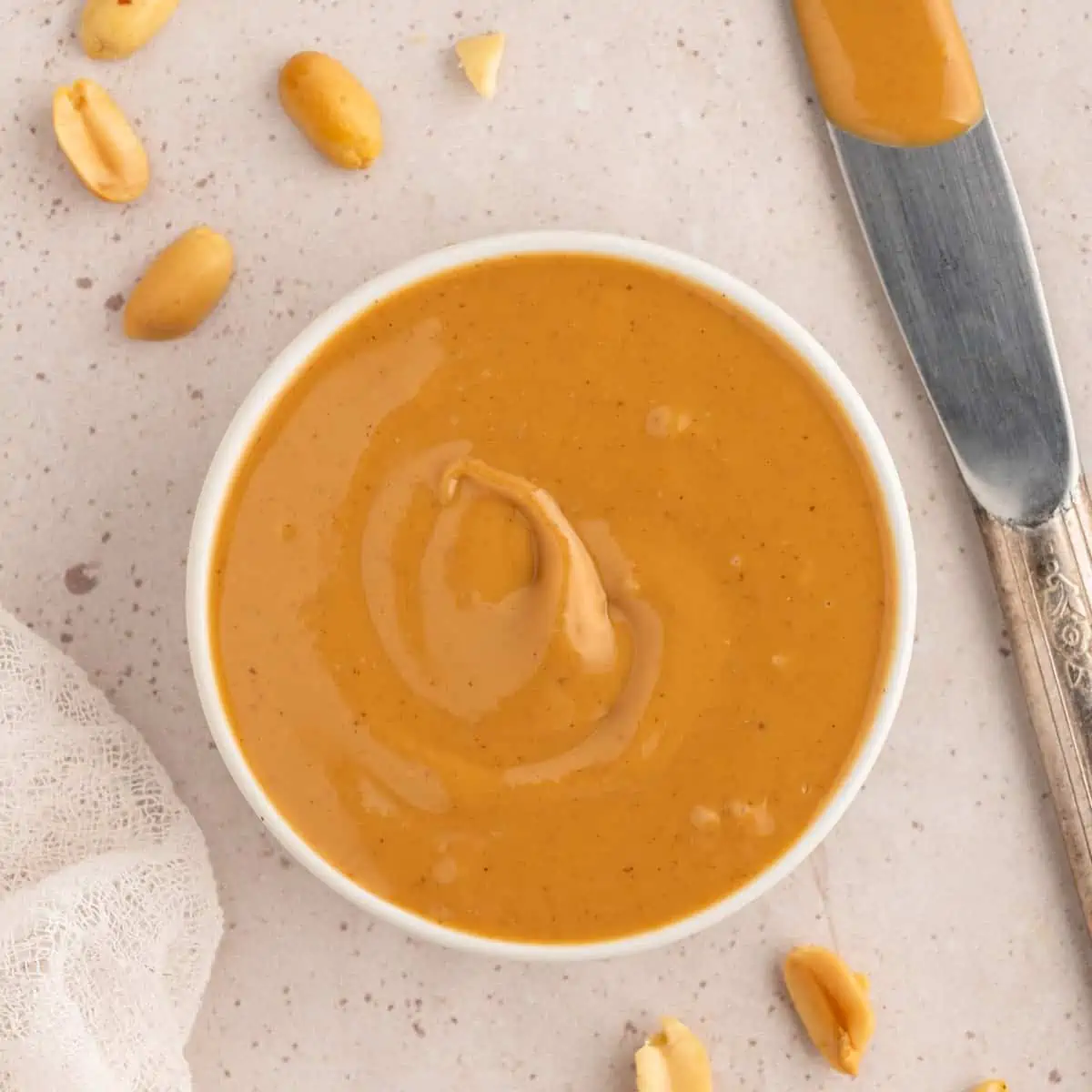 Homemade peanut butter in a white dish with peanuts.