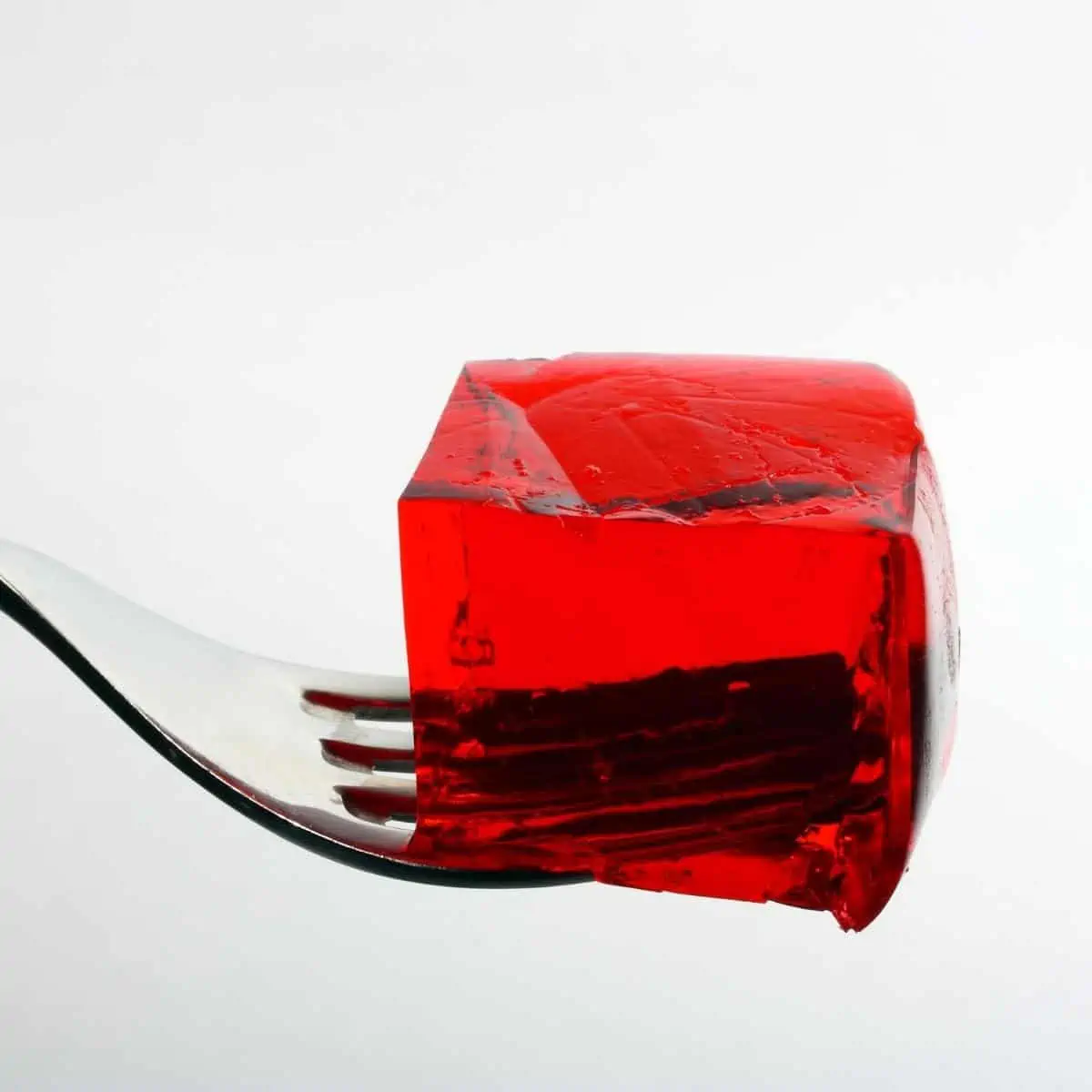 Red cube of jello balancing on a fork. 