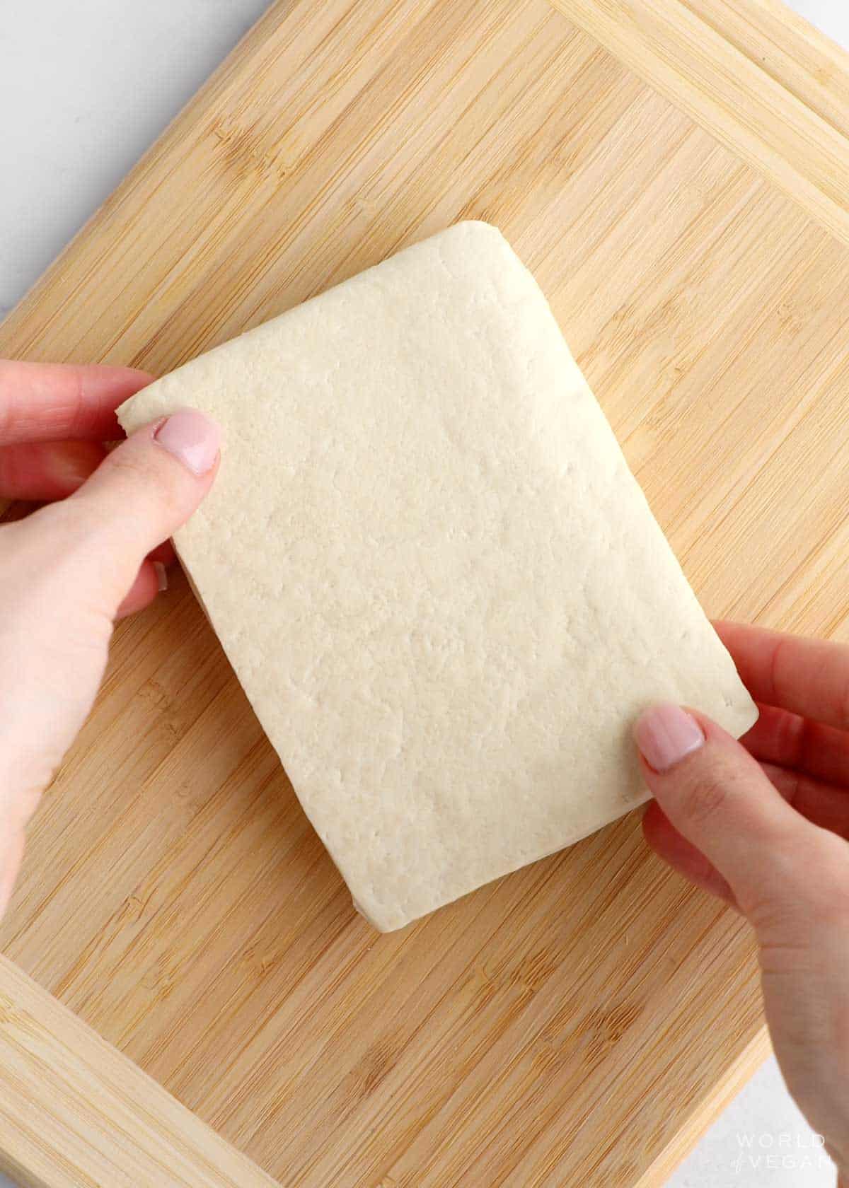 Block of extra firm tofu on a cutting board. 