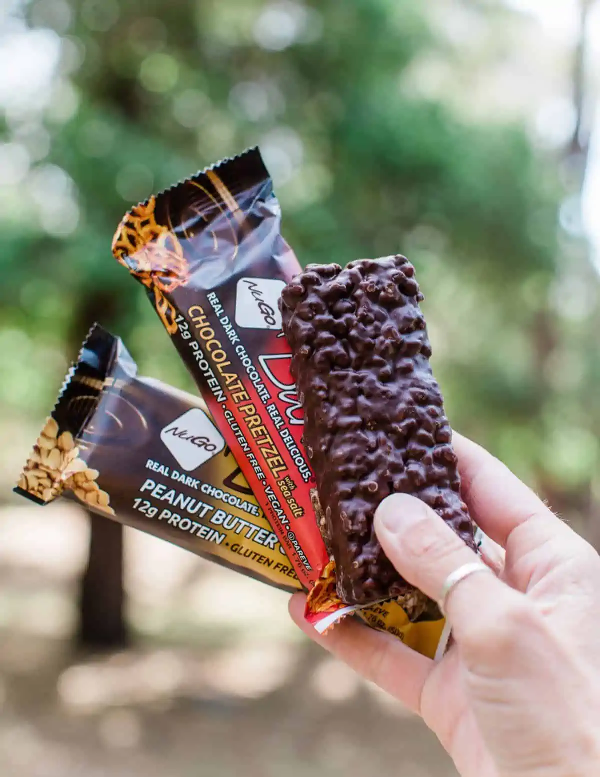 Woman's hand holding out three vegan Nugo protein bars.