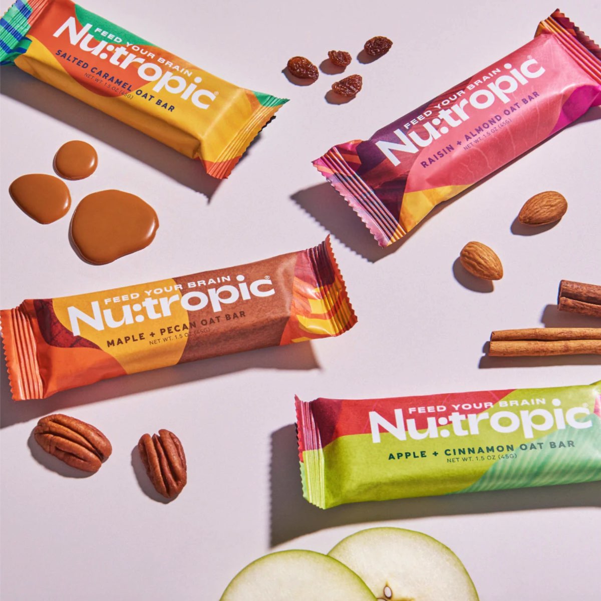 Four varieties of nutropic energy bars made from nuts and plant-based ingredients on a pink table. 