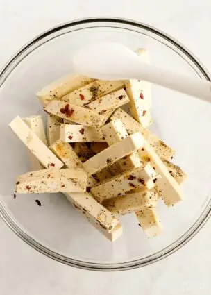 Adding spices, cornstarch, and nutritional yeast to the tofu fries in a mixing bowl.