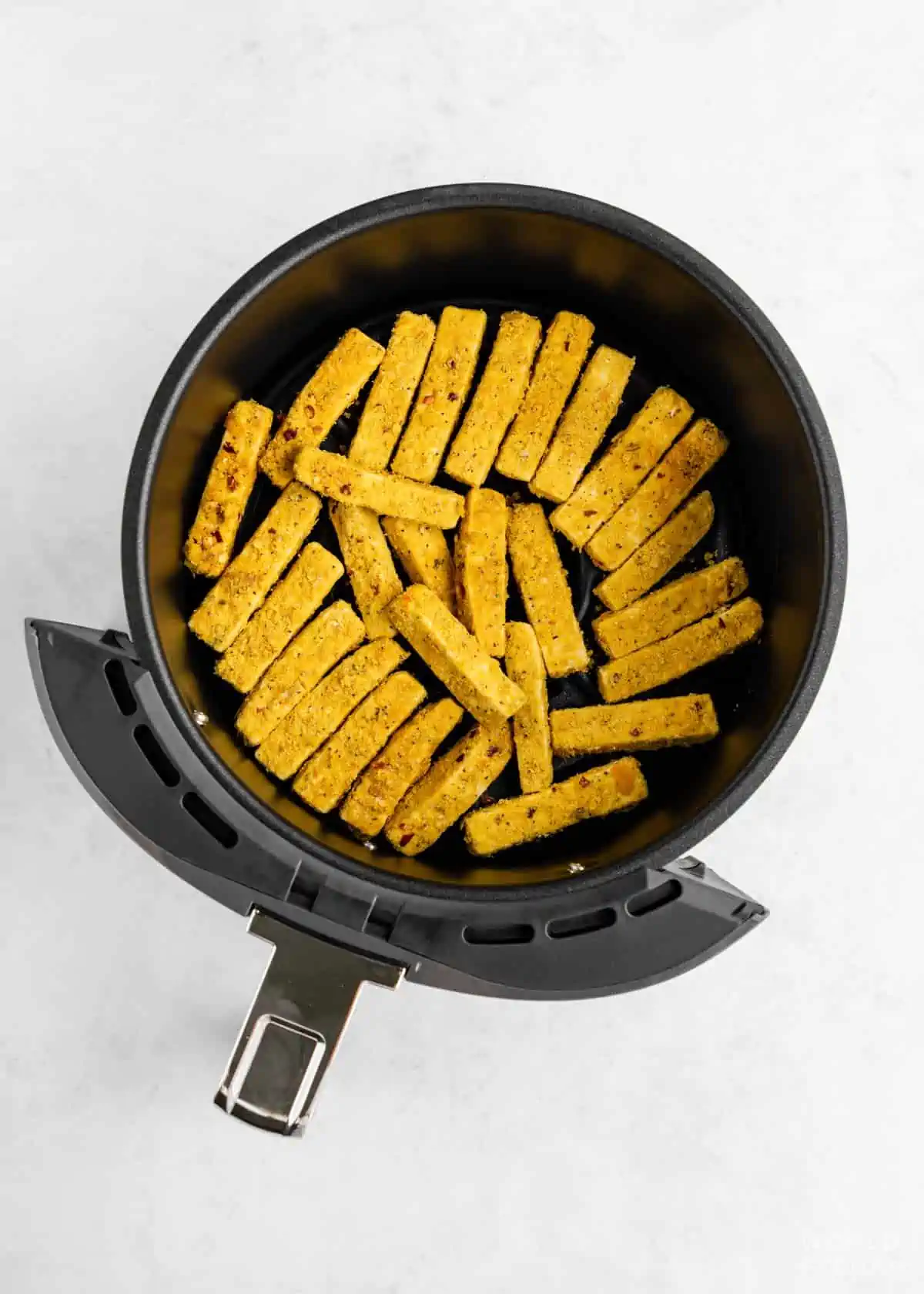 Tofu fries placed flat in an air fryer basket. 