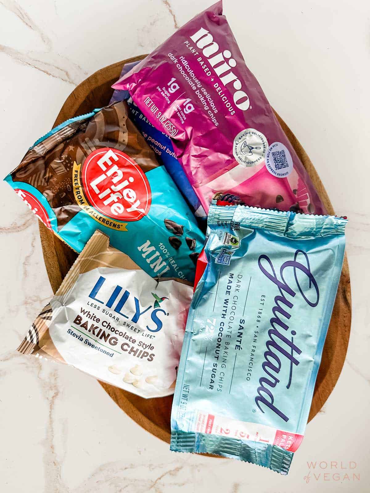 Flatlay showing several different brands of vegan chocolate chips including Guittard, Lily's, Enjoy Life, and Miiro.