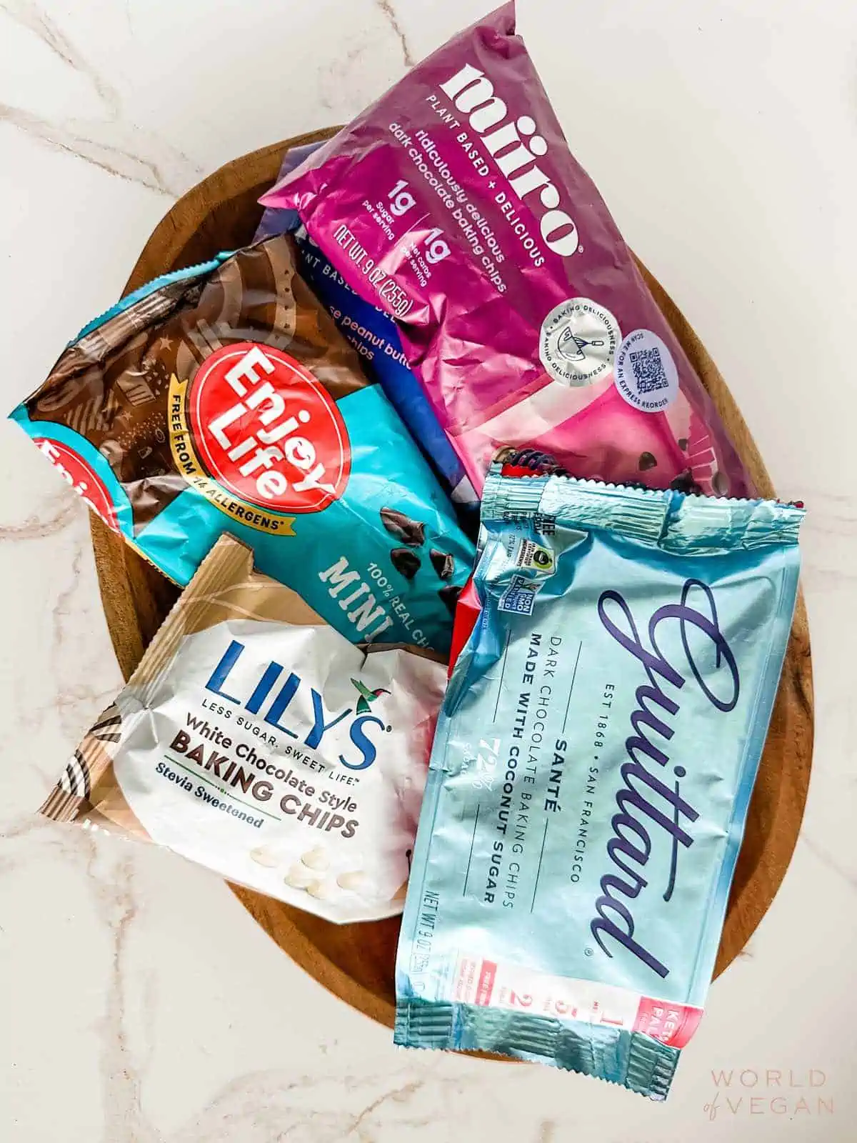 Flatlay showing several different brands of vegan chocolate chips including Guittard, Lily's, Enjoy Life, and Miiro. 