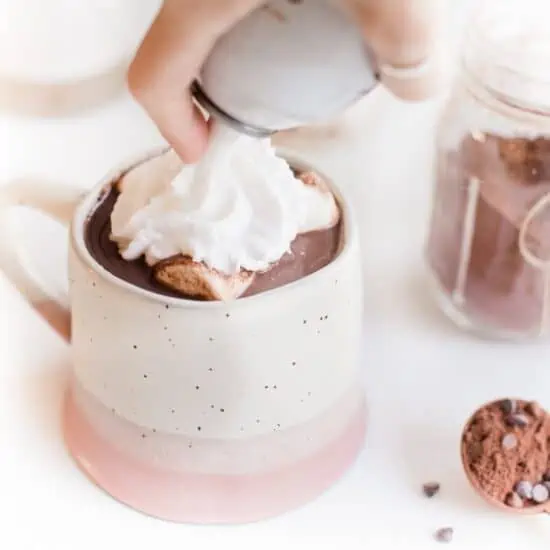 Swirling fluffy vegan whipped cream from a can onto a mug of dairy-free hot cocoa.