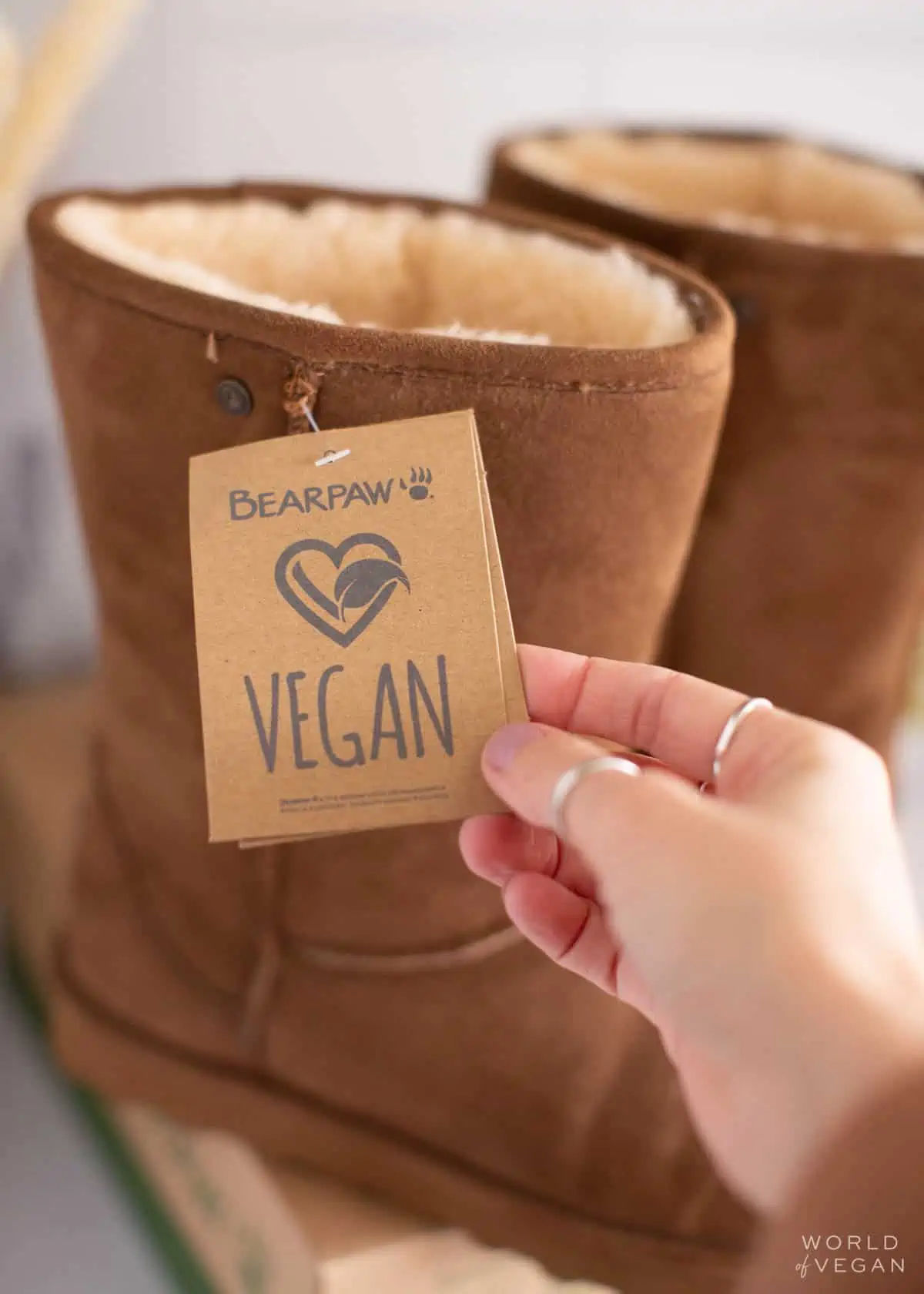 Woman holding out a vegan label tag on a pair of UGG boots. 