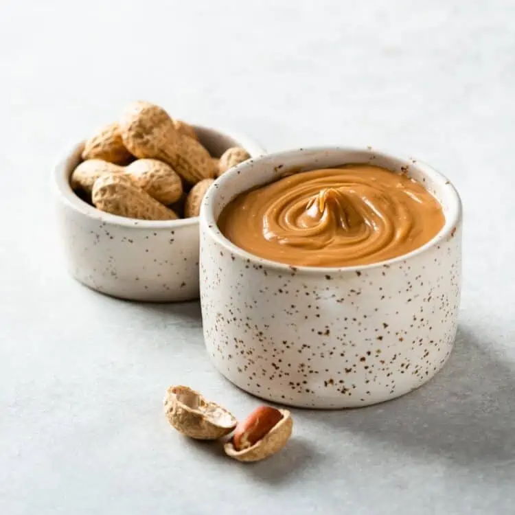 Creamy vegan peanut butter in a rustic spotted ceramic dish with whole peanut next to it.