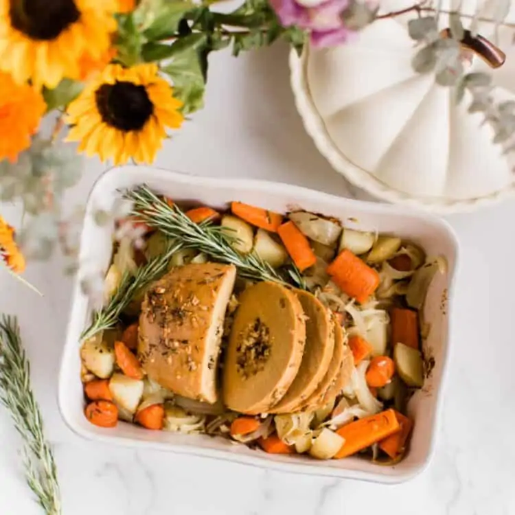 Vegan tofurky turkey roast with thanksgiving pumpkin pie and fall flowers on a table.
