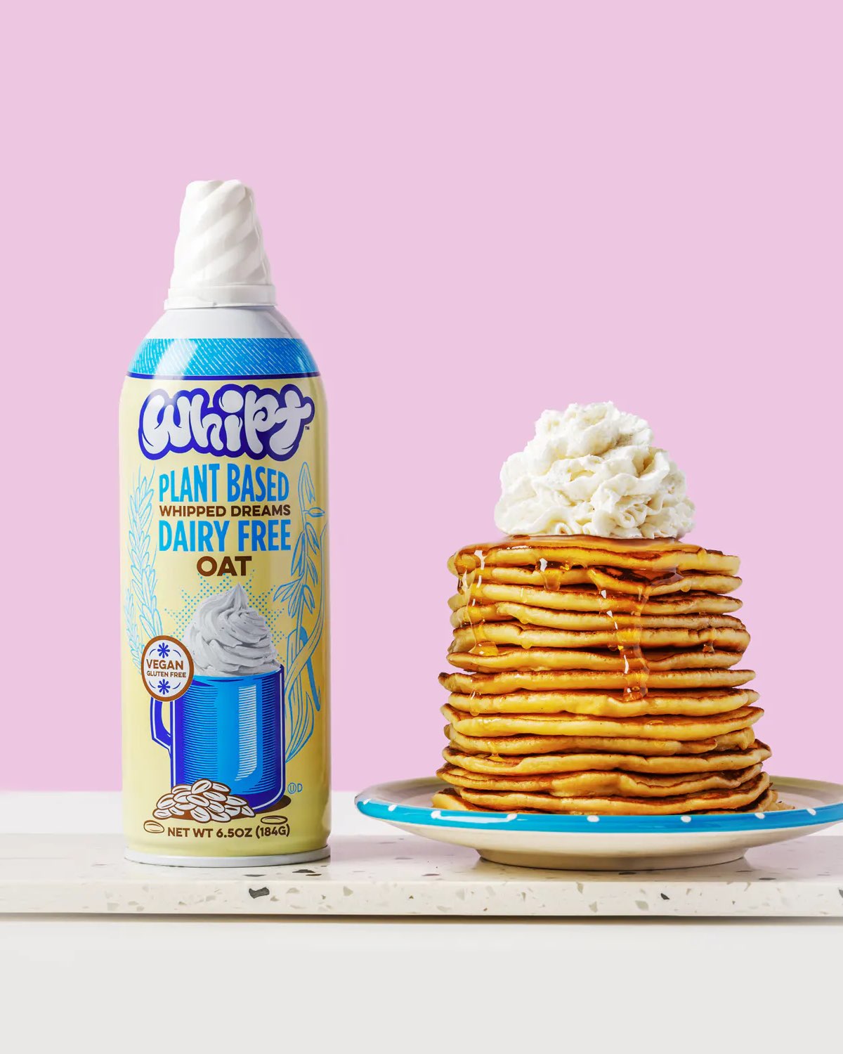 A spray can bottle of Whipt oat whipped cream  next to a stack of vegan pancakes. 