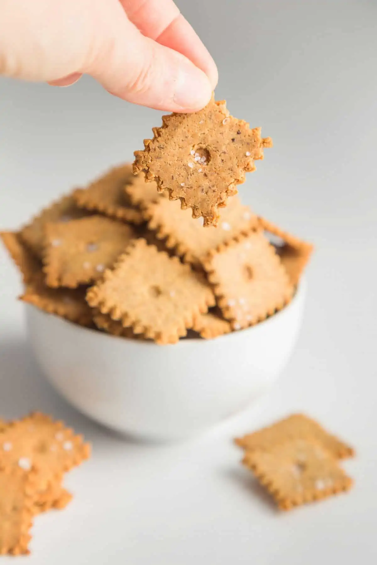 A close-up shot of almond flour cracker. There is a full bowl of crackers in the background.