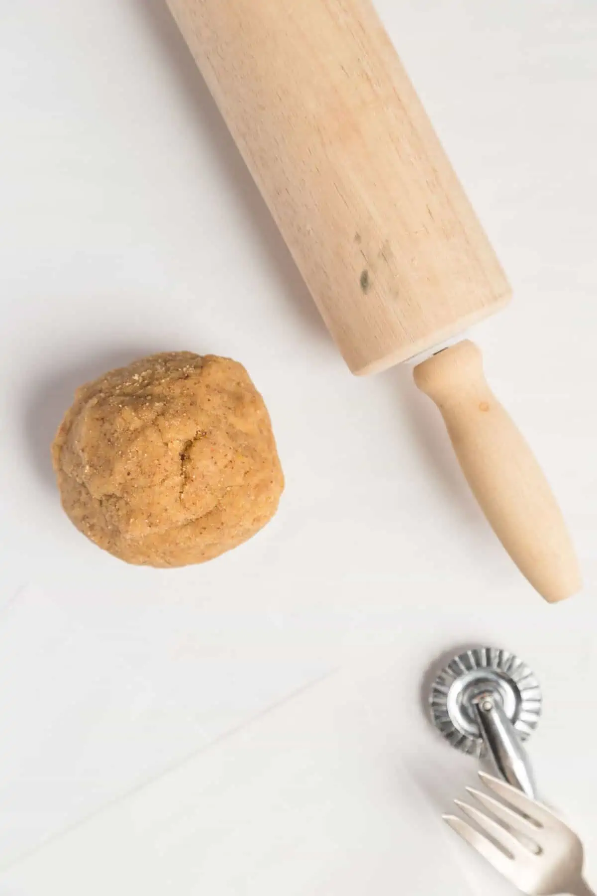 A top-down shot of almond flour cracker dough rolled into a ball with a rolling pin next to it.