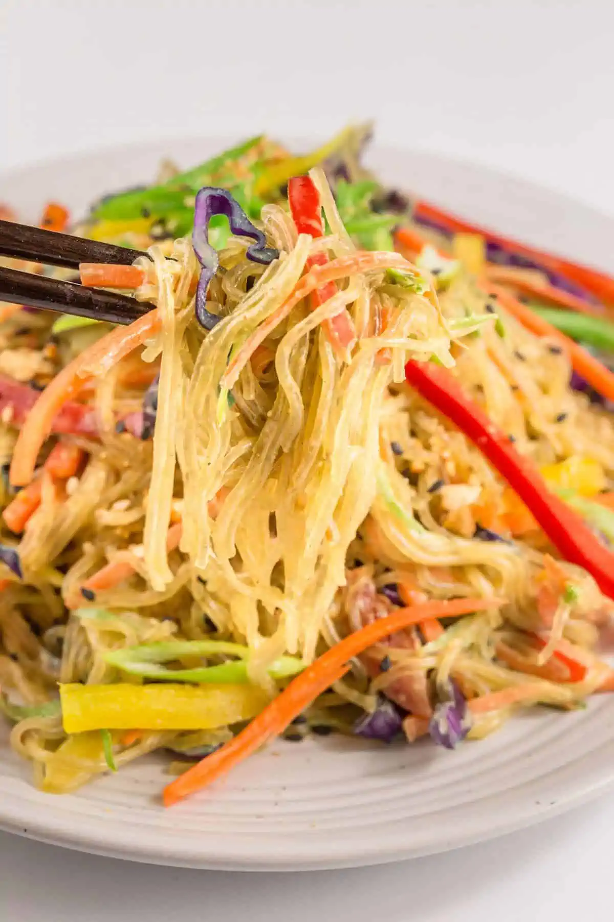 Chopsticks holding up kelp noodle salad of a plate of it.