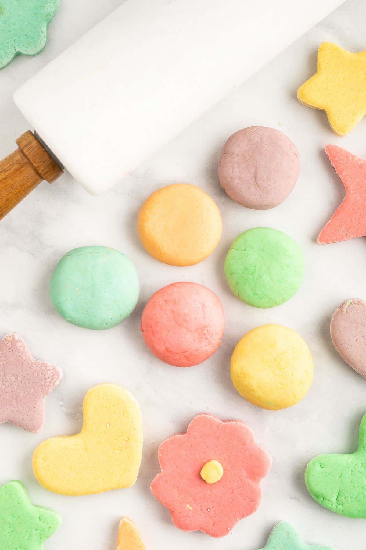 Rainbow colored balls of homemade playdough with various colorful shapes scattered around.