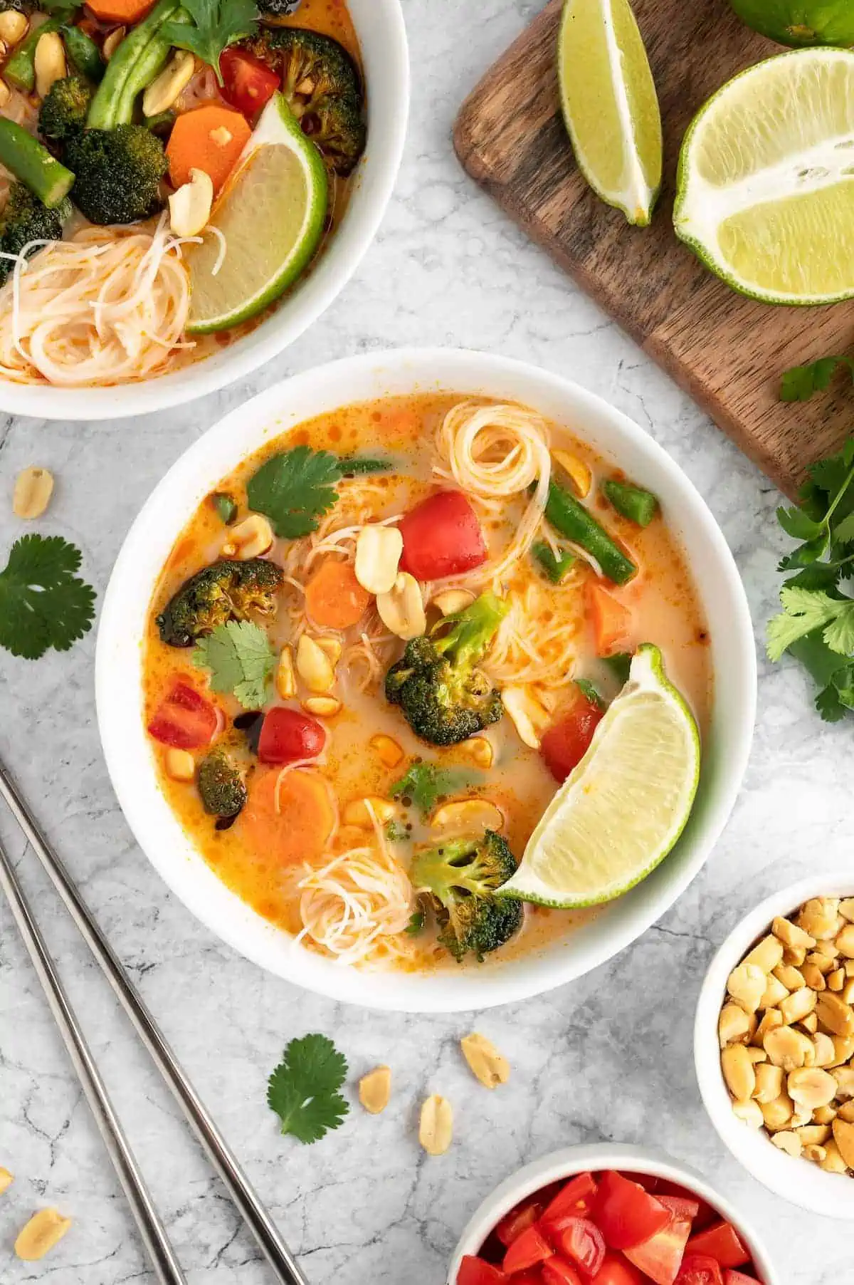 Two bowls of Thai curry with lime wedges against a marble background.