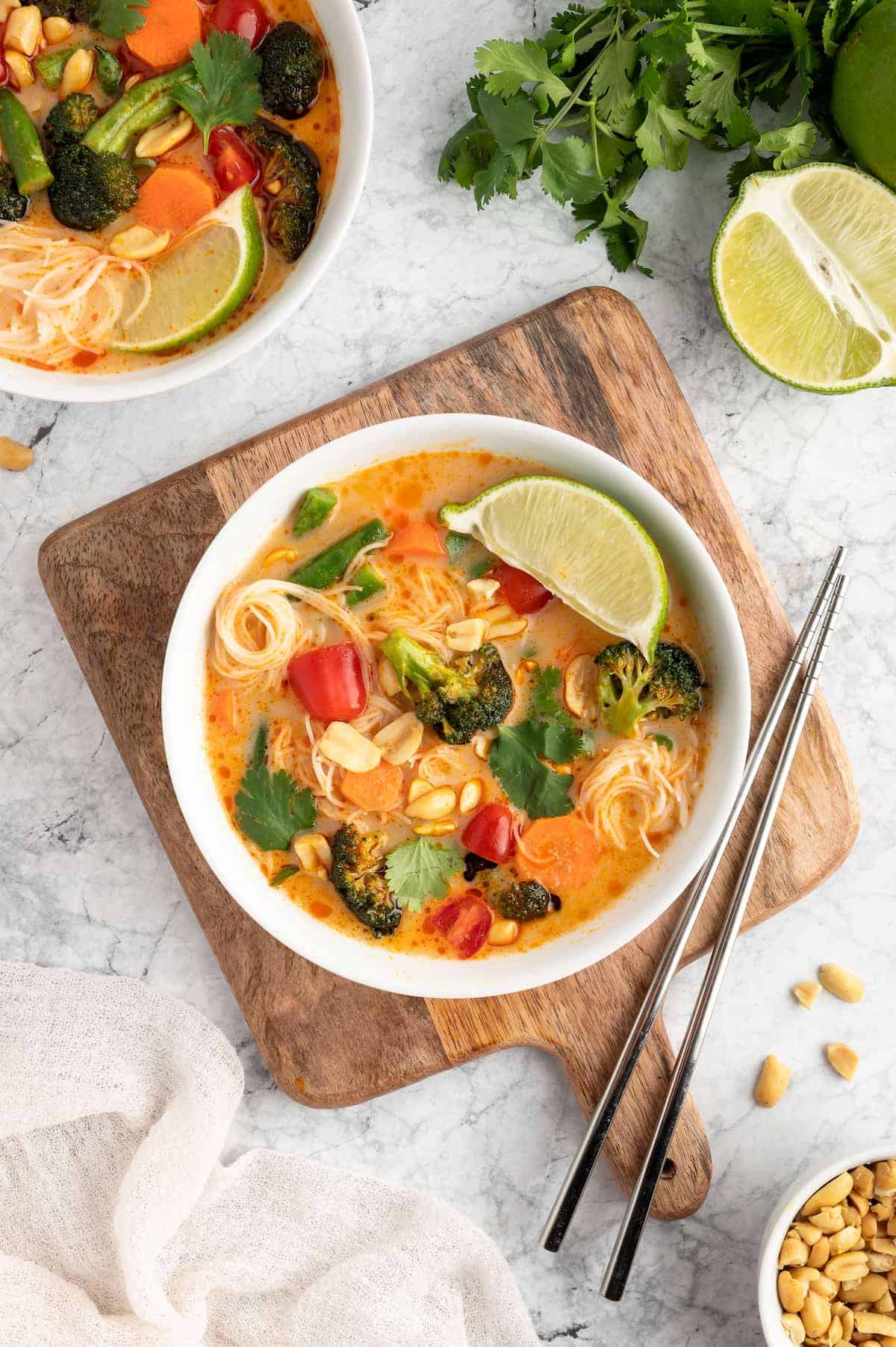 Thai curry in a white bowl on a wooden serving tray, with chopsticks and a white napkin to the side.