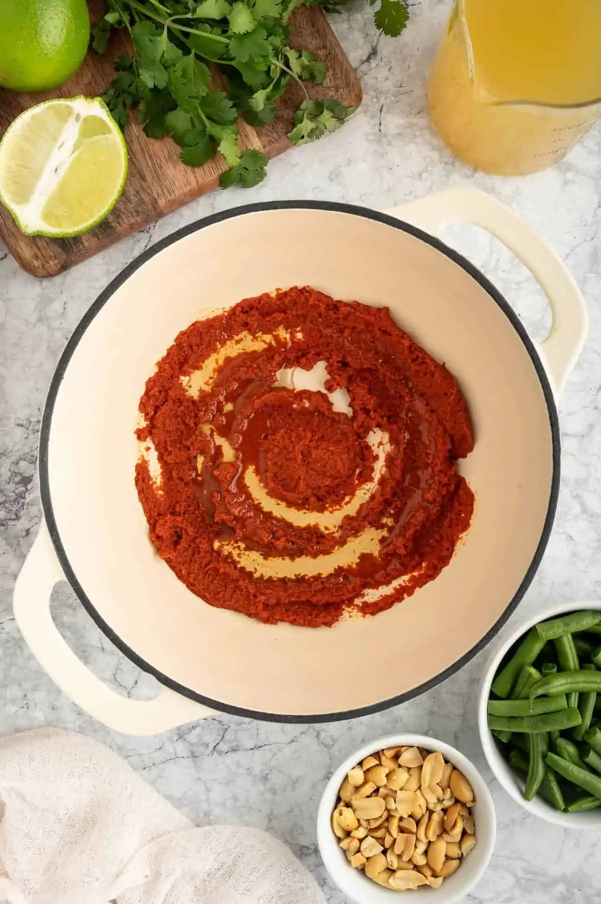 A top-down shot of curry paste and oil in a large white-enameled pot.