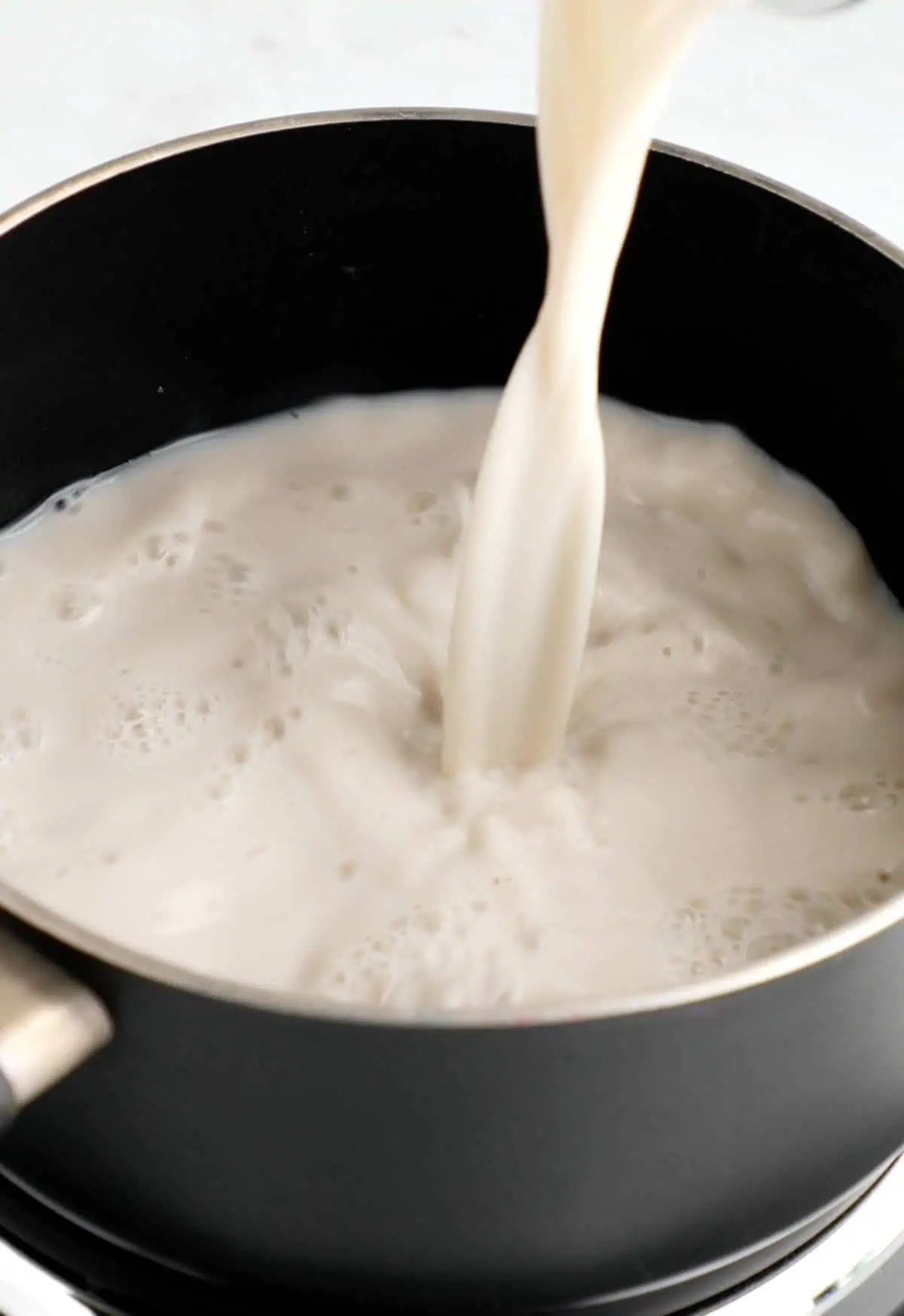 Plant milk being poured in a saucepan.
