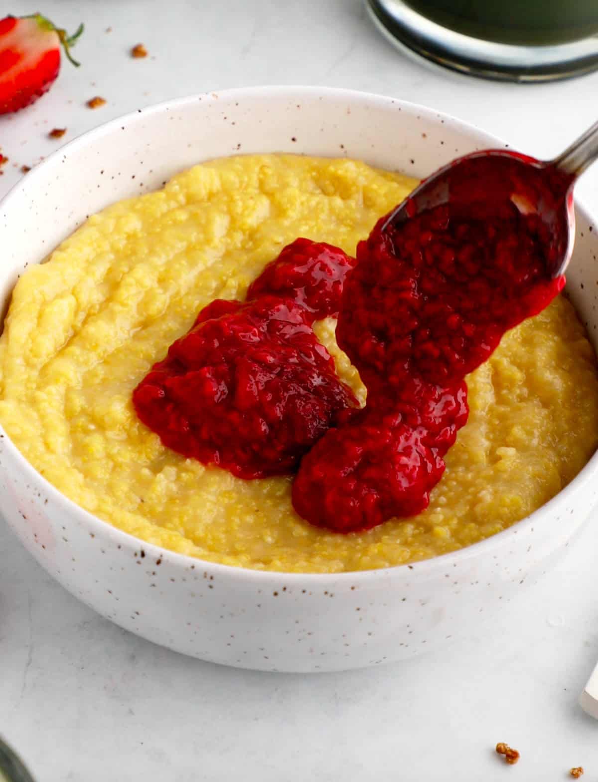 A bowl of vegan grits with a spoon adding the berry compote on top.
