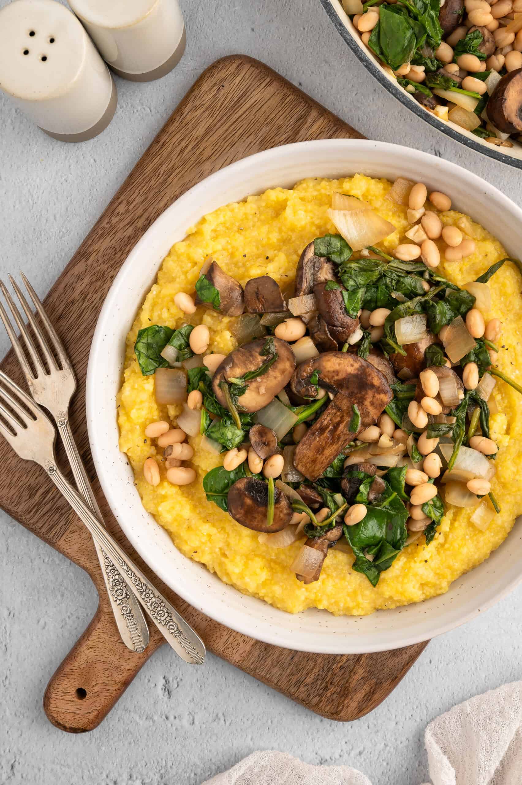 A bowl of vegan polenta and greens on a wooden board.