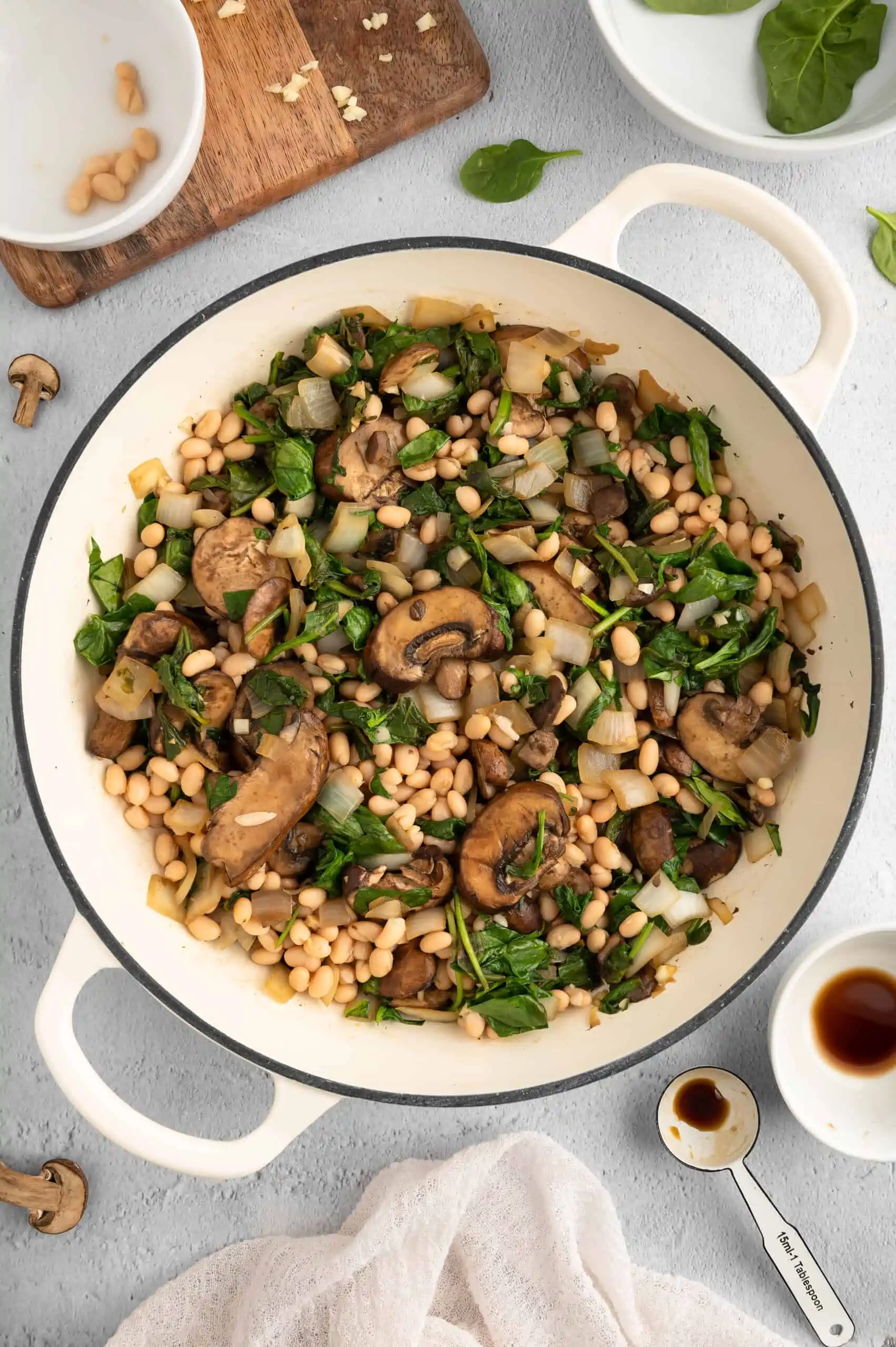 A pot with mushrooms, greens, and navy beans.
