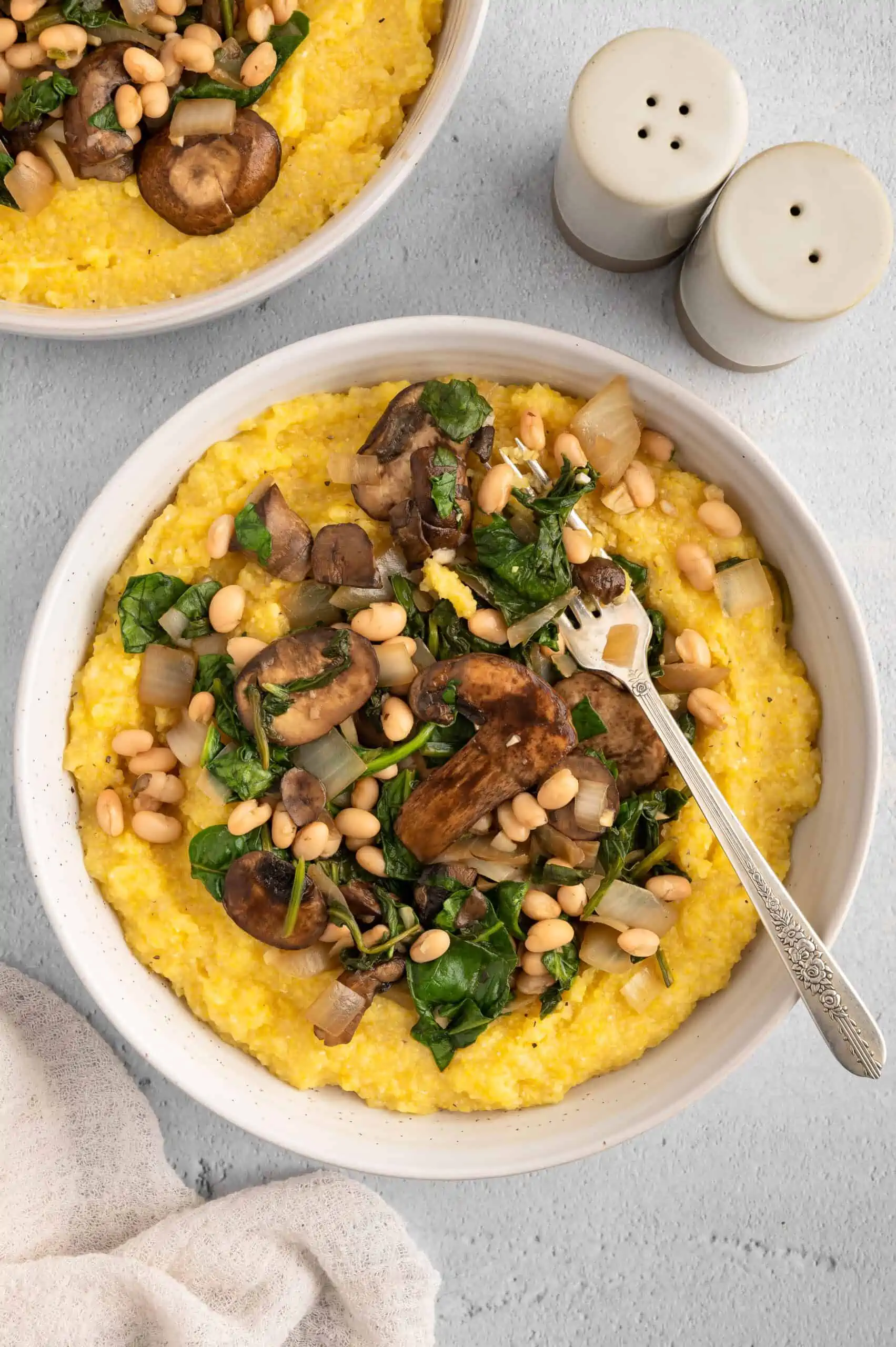 A bowl of vegan polenta and greens with salt and pepper shakers.