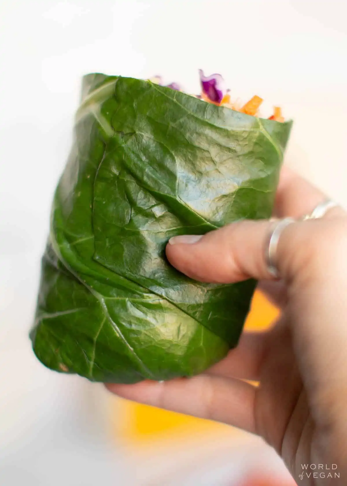 Hand holding a collard green wrap that has been sliced in half.