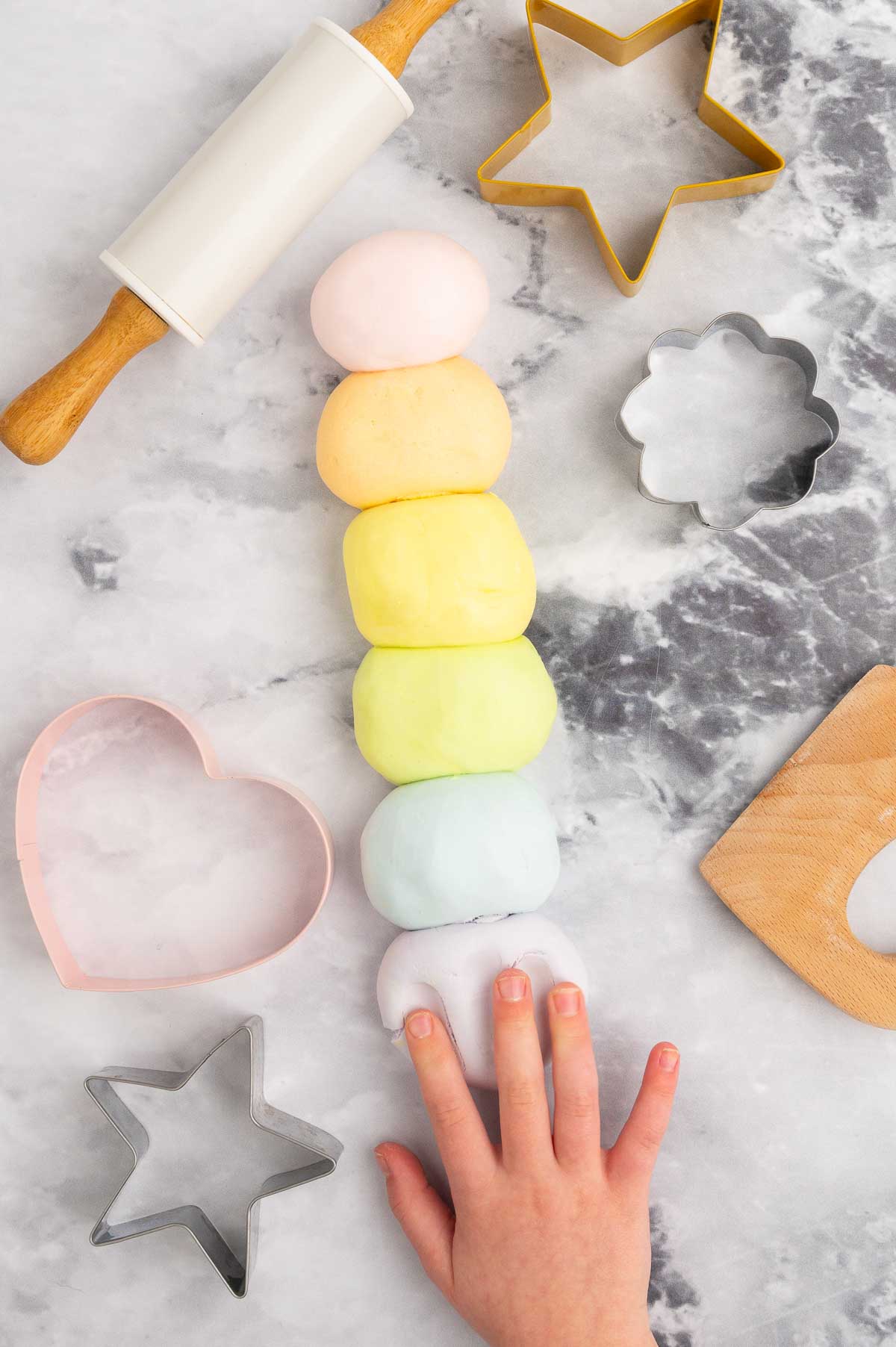 Cloud dough with colors in a row, with a child's hand reaching for it.