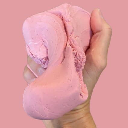 Vegan woman holding up homemade diy pink cloud dough made with conditioner and cornstarch.