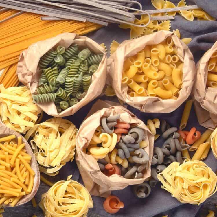 Paper bags filled with different types of healthy noodles with various pasta noodles scattered around.