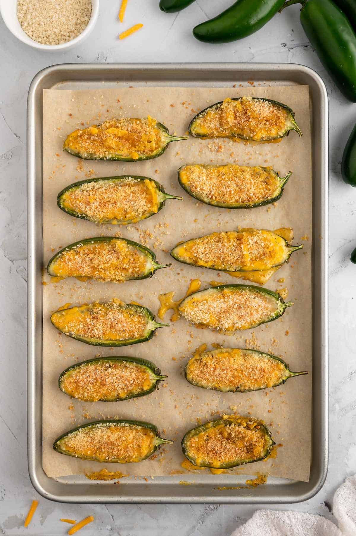 Jalapeno poppers on a baking sheet, after coming out of the oven. The peppers are browned and bubbly.